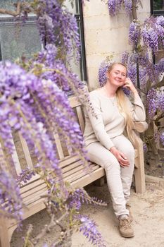 a beautiful middle-aged woman sits on a bench in the thickets of blooming wisteria and meditates happy. High quality photo
