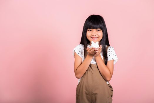 Asian little kid 10 years old holding piggy bank and looking at camera at studio shot isolated on pink background, Happy child girl lifestyle smiling with is full piggybank, Personal money savings