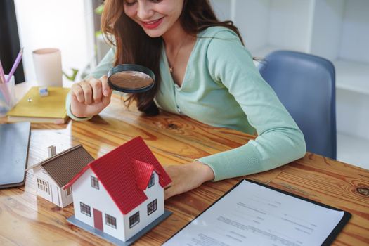 The client holds a magnifying glass to select a house model, inspect the concept of a home before making a decision to invest, make a loan, get insurance and sign important documents with the bank