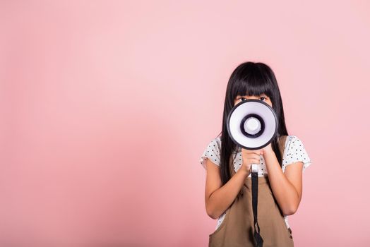Asian little kid 10 years old shouting by megaphone at studio shot isolated on pink background, Happy child girl lifestyle she screeching through in megaphone announces discounts