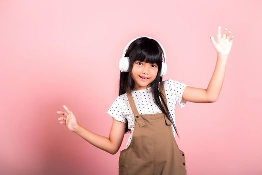 Asian little kid 10 years old smiling listening music wearing wireless headset and dancing in studio shot isolated on pink background, Child girl funny listen music with headphones