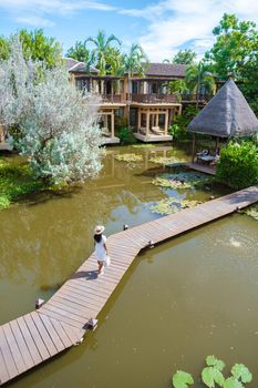 Asian women walking at a wooden pier at a tropical resort in Asia. Asian woman with a hat at a wooden pier in a pond