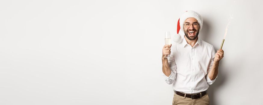 Winter holidays and celebration. Handsome bearded man having New Year party, holding firework sparkle and champagne, wearing santa hat, white background.