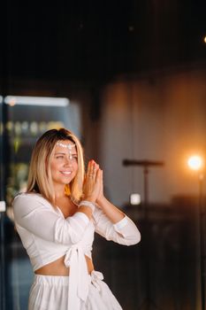 Portrait of a smiling girl in a white dress with her palms clasped in front of her.