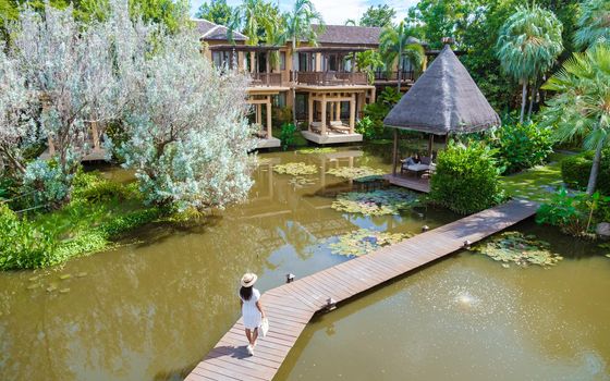 Asian women walking at a wooden pier at a tropical resort in Asia. Asian woman with a hat at a wooden pier in a pond