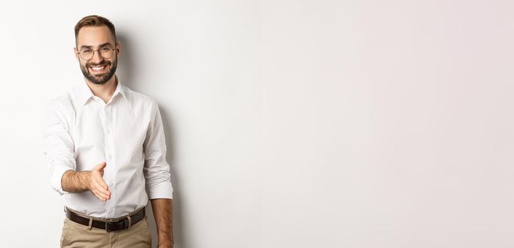 Confident businessman extending hand for handshake, greeting business partner and smiling, standing over white background.