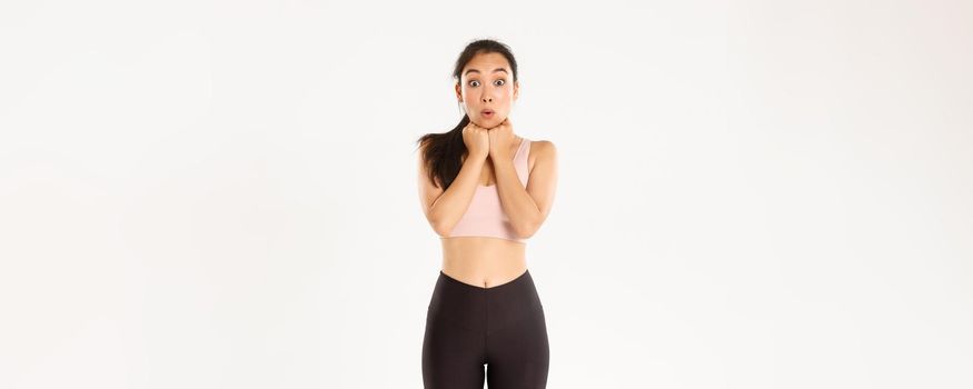 Sport, wellbeing and active lifestyle concept. Excited and amazed, thrilled asian fitness girl in activewear looking at discount banner, special offer advertisement, standing white background.
