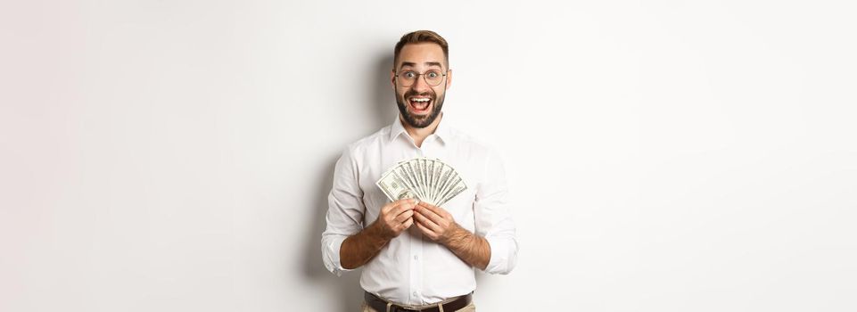 Excited handsome man holding money, rejoicing of winning cash prize, standing over white background.