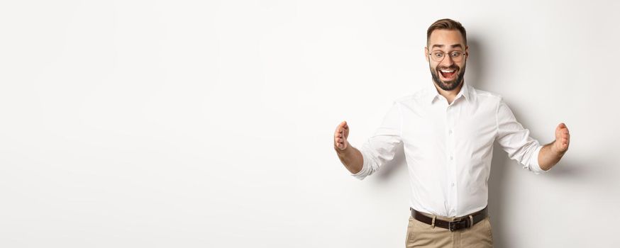 Amazed businessman showing big object, describe something large and looking excited, standing over white background.