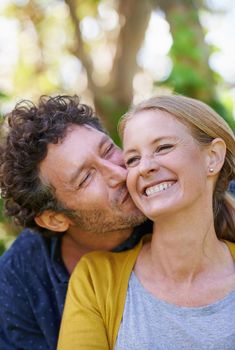 Giving her a big kiss on the cheek. an affectionate husband and wife standing outdoors