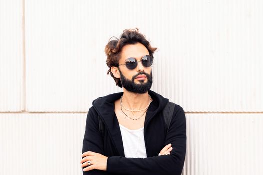 beautiful young man with sunglasses leaning in a white wall, concept of urban lifestyle and stylish clothing, copy space for text
