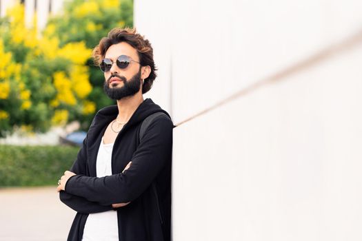 beautiful young man with sunglasses leaning in a white wall, concept of urban lifestyle and stylish clothing, copy space for text