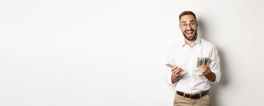 Handsome business man looking excited while counting money, standing over white background.
