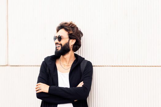 beautiful young man with sunglasses smiling happy leaning in a white wall, concept of urban lifestyle and stylish clothing, copy space for text