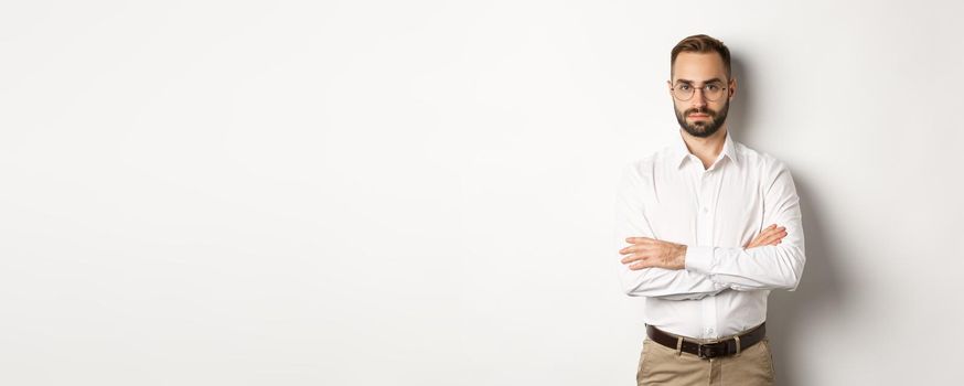 Confident businessman in glasses looking at camera, cross arms on chest, standing over white background.