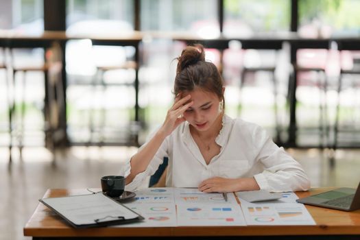 Stressed Asian business woman worry with many document on desk at office.