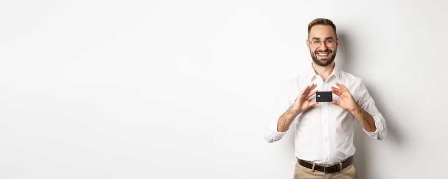 Handsome businessman holding a card, smiling satisfied, standing over white background.