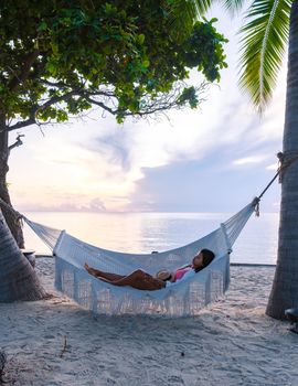 women watching sunrise in a White hammock under palm trees at a tropical beach in Thailand Hua Hin. Tropical beach in Huahin with a hammock by the ocean on a white beach