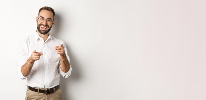 Satisfied businessman pointing fingers at camera, praising you, approve or like something, white background.