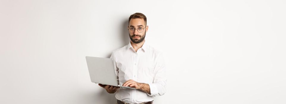 Business. Young handsome businessman working on laptop, doing job on computer, standing over white background.