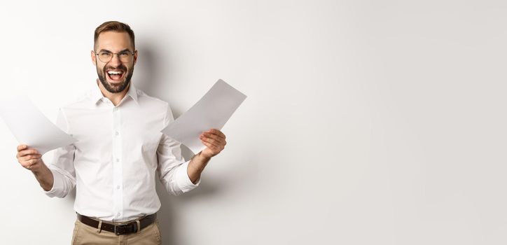 Angry boss disappointed with documents, shouting mad and aggressive, standing over white background.