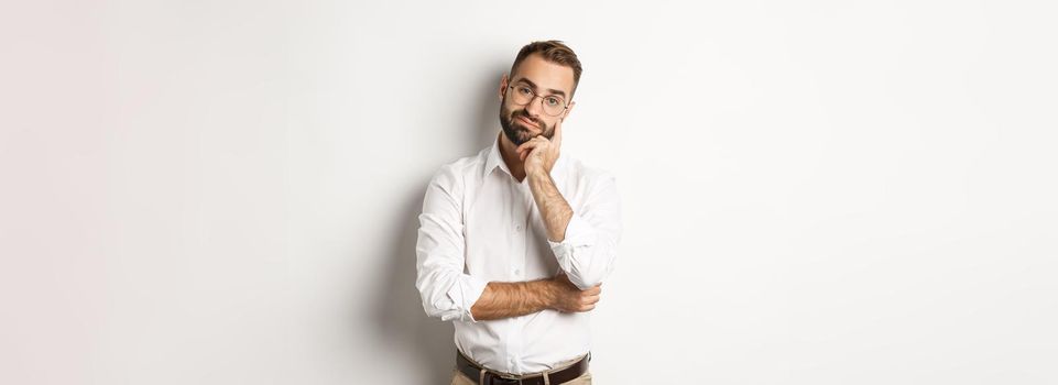 Unamused bearded man in glasses looking displeased at camera, standing moody over white background.