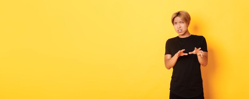 Portrait of disgusted picky asian guy, refusing and grimacing, standing yellow background.