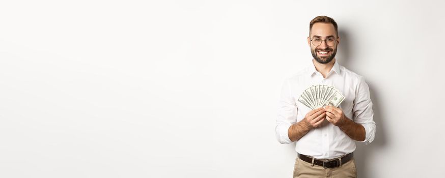 Smiling handsome man holding money, showing dollars, standing over white background. Copy space