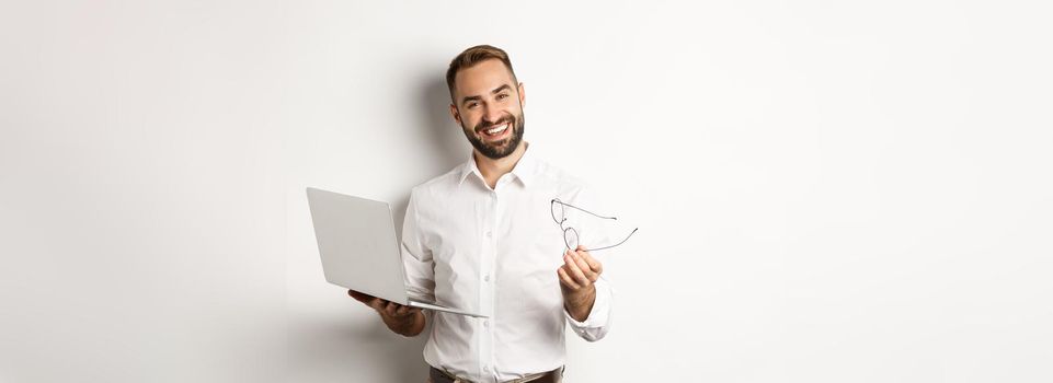 Satisfied businessman praising good job while checking laptop, standing over white background. Copy space
