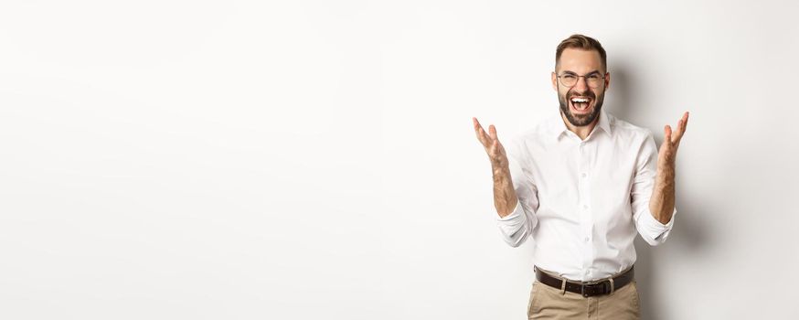 Frustrated and angry man screaming in rage, shaking hands furious, standing over white background. Copy space