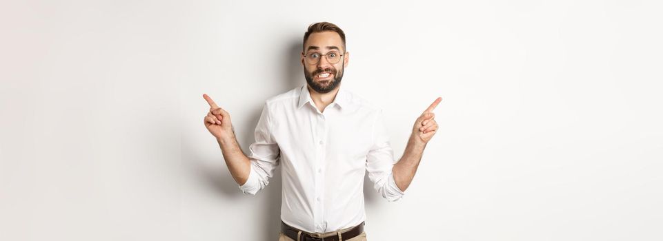 Indecisive businessman pointing sideways, showing two variants, struggling make choice, standing over white background.