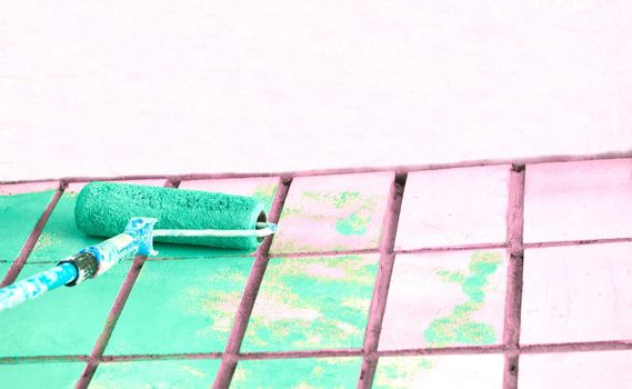 an implement with a handle, consisting of bristles, hair, or wire set into a block, used for cleaning, applying a liquid to a surface. Roller painting pale pink wall surface with green emerald paint