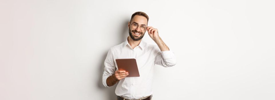 Confident business man working on digital tablet, smiling happy, standing over white background.