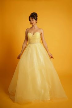 Portrait of a beautiful middle-aged woman in a yellow dress, her hair pulled up against a yellow background.