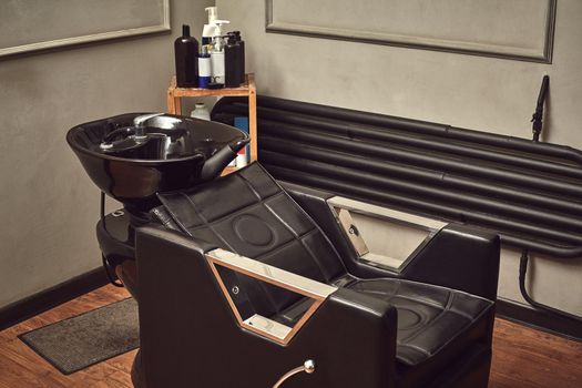Black leather seat with wash basin in a barbershop interior with towels and shampoo on the side. Fashionable haircut from a professional