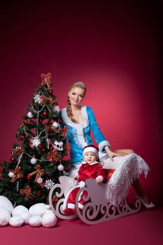 christmas girl and baby santa claus portrait on red with fir tree