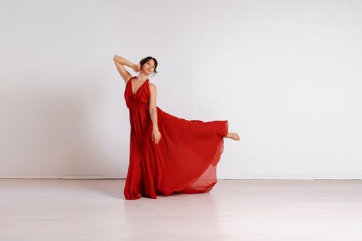 Dancer in a red flying dress. Woman ballerina dancing on a white studio background.