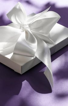 Anniversary celebration, shop sale promotion and bridal surprise concept - Luxury holiday white gift box with silk ribbon and bow on violet background, luxe wedding or birthday present