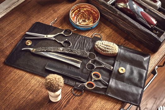 Hairdresser tools on wooden background. Top view on wooden table with scissors, comb, hairbrushes and hairclips, trimmer. Barbershop, manhood concept