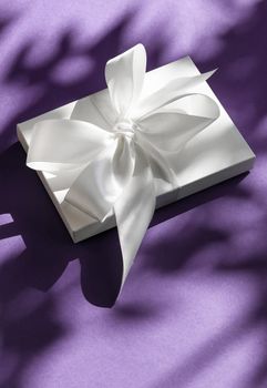 Anniversary celebration, shop sale promotion and bridal surprise concept - Luxury holiday white gift box with silk ribbon and bow on violet background, luxe wedding or birthday present