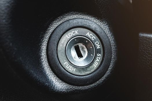 Car ignition lock under the steering wheel in a black interior.