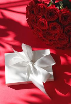 Happy holidays, luxe shopping and love gifts concept - Luxury holiday silk gift box and bouquet of roses on red background, romantic surprise and flowers as birthday or Valentines Day present