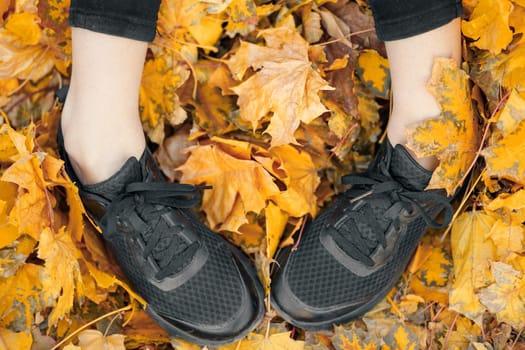 Top view of casual woman black sneakers in the autumn leaves.