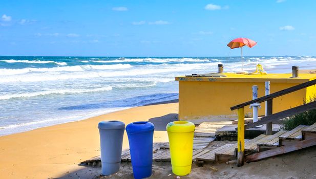 Alicante, Spain- September 18, 2022:Colorful Recycling bins on the beach and red umbrella on the background