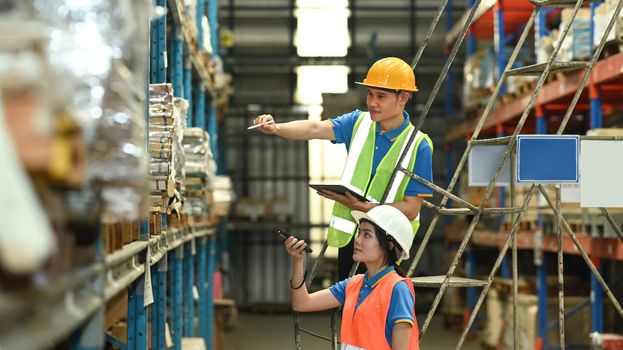 Warehouse workers checking inventory boxes with barcode scanner on shelf in a large warehouse.