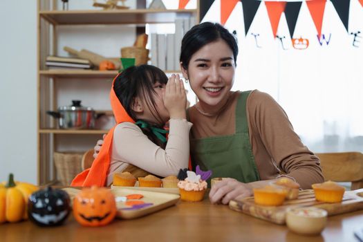 Young girl and mother at Halloween making treats and cupcake on table. Happy Halloween day.