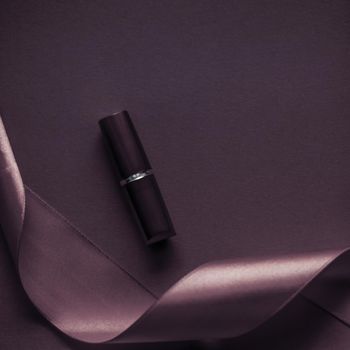 Cosmetic branding, glamour lip gloss and shopping sale concept - Luxury lipstick and silk ribbon on dark purple holiday background, make-up and cosmetics flatlay for beauty brand product design