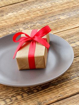 Gift box with red ribbons on the plate on the old wooden boards. Concept of giving a gift on holidays. Top view.