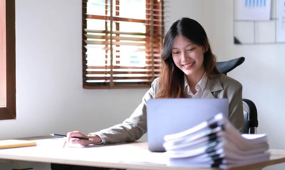 Beautiful Asian businesswoman analyzes charts using laptop calculator at the office..