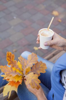 Close-up view of young woman with a cup of coffee and dry autumn leaves in her hands. Top view. Autumn composition.